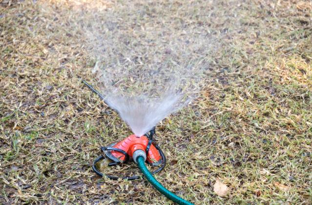 A water sprinkler sprays water on a dry lawn in a garden during winter season