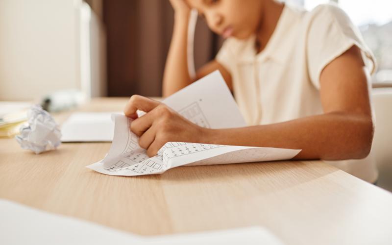 Anxious child crumpling homework while struggling with school work.