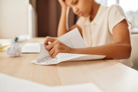 Anxious child crumpling homework while struggling with school work.